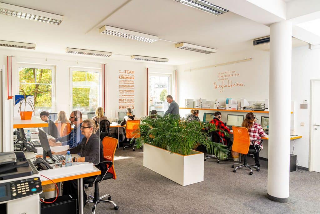 Office with several call centre employees working at desks and using orange chairs.