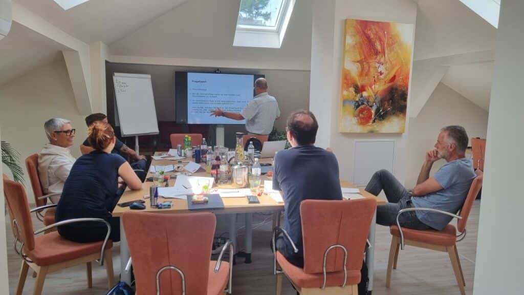A group of people are sitting at a table in a conference room during a presentation.